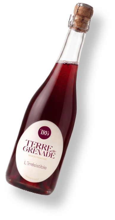Bouteille inclinée de liquide rouge, bouchée liège et muselet. L'étiquette ronde lit : "TERRE de GRENADE MAISON FRANÇAISE L'Irrésistible FABRIQUÉ SUR LE DOMAINE".