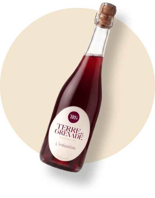 A tilted bottle of red sparkling beverage, with the label "TERRE de GRENADE MAISON FRANÇAISE The Irresistible INNOVATIVE PRODUCT" on a light-colored circular background.