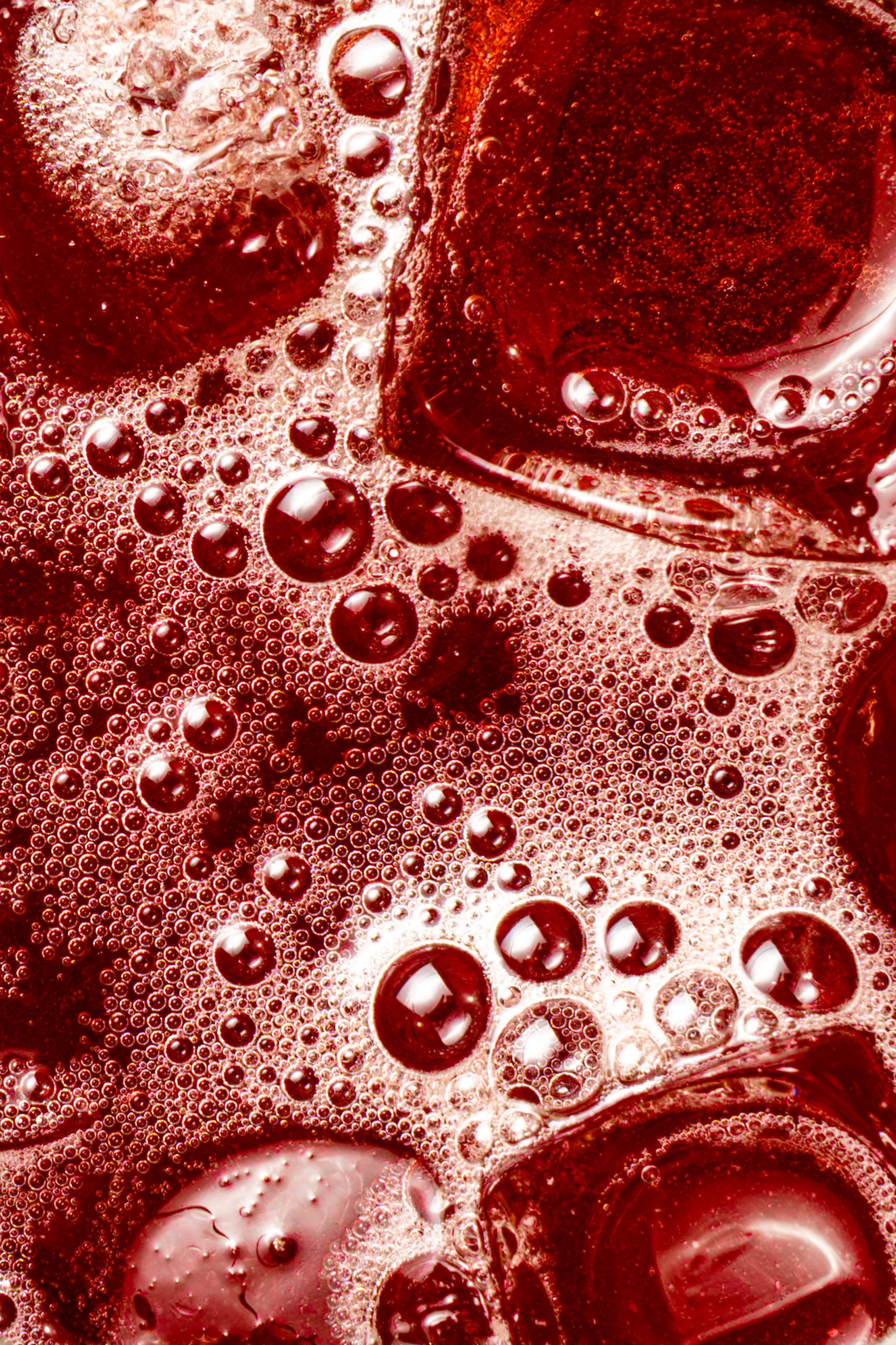Liquide pétillant rouge-brun avec des bulles de tailles variées se formant à sa surface et des glaçons à demi fondus.