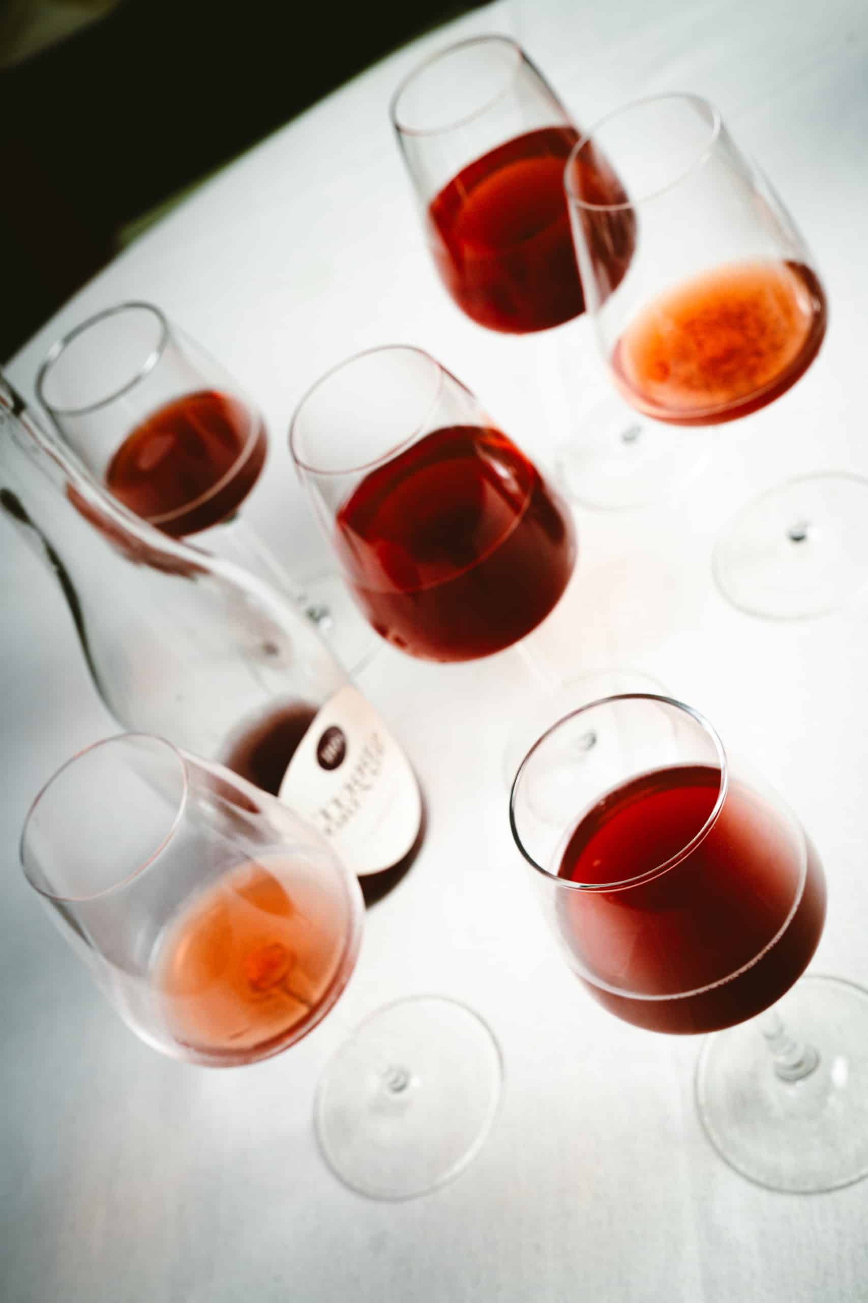 Verres à vin remplis de rouge et rosé, avec une bouteille sur une table blanche. L'étiquette: "DOMAINE DE LA RÉCOLTE 2018".